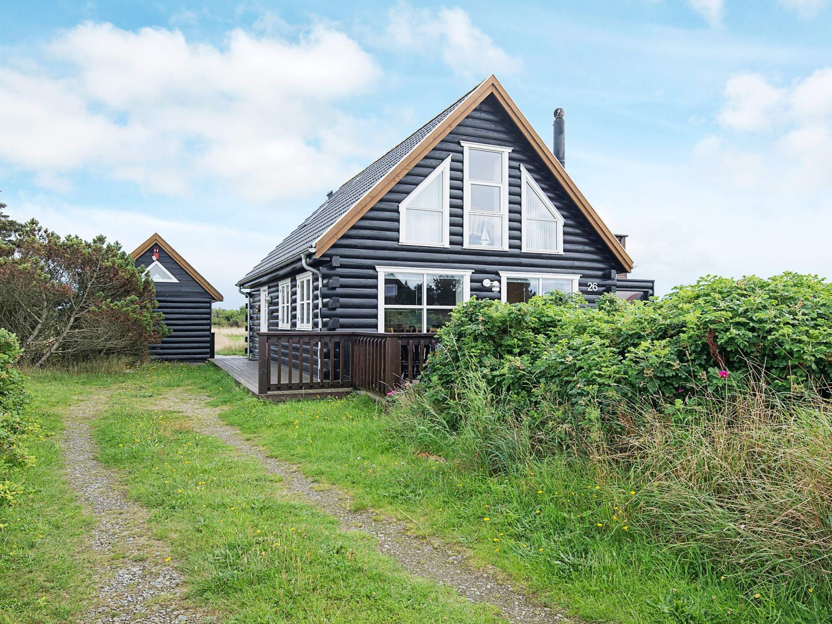 A log cabin with a wooden deck and a gravel path leading to it.