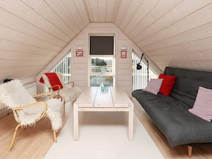 A cozy attic room with a white table, a grey sofa with red cushions, and a white chair with a red throw.