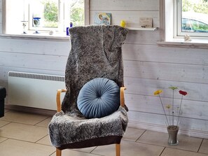 A chair with a furry throw blanket and a blue cushion, positioned next to a radiator and a vase with flowers.