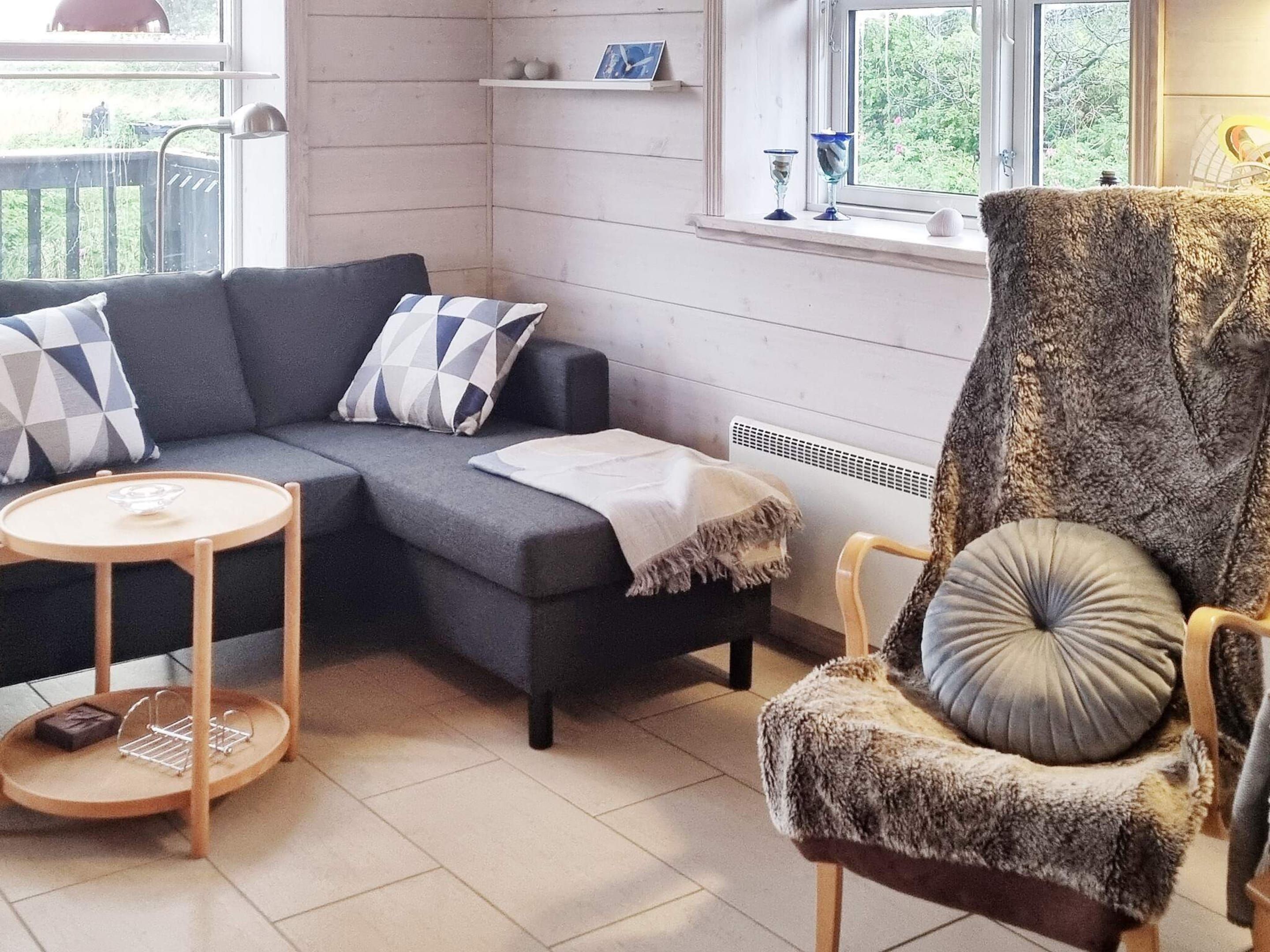 A living room with a sofa, a chair, a small round table, and a window with a view of greenery.