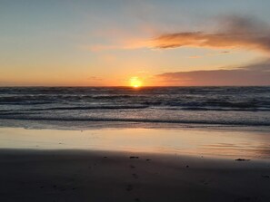 A beach with the sun setting over the ocean, waves gently lapping at the shore.