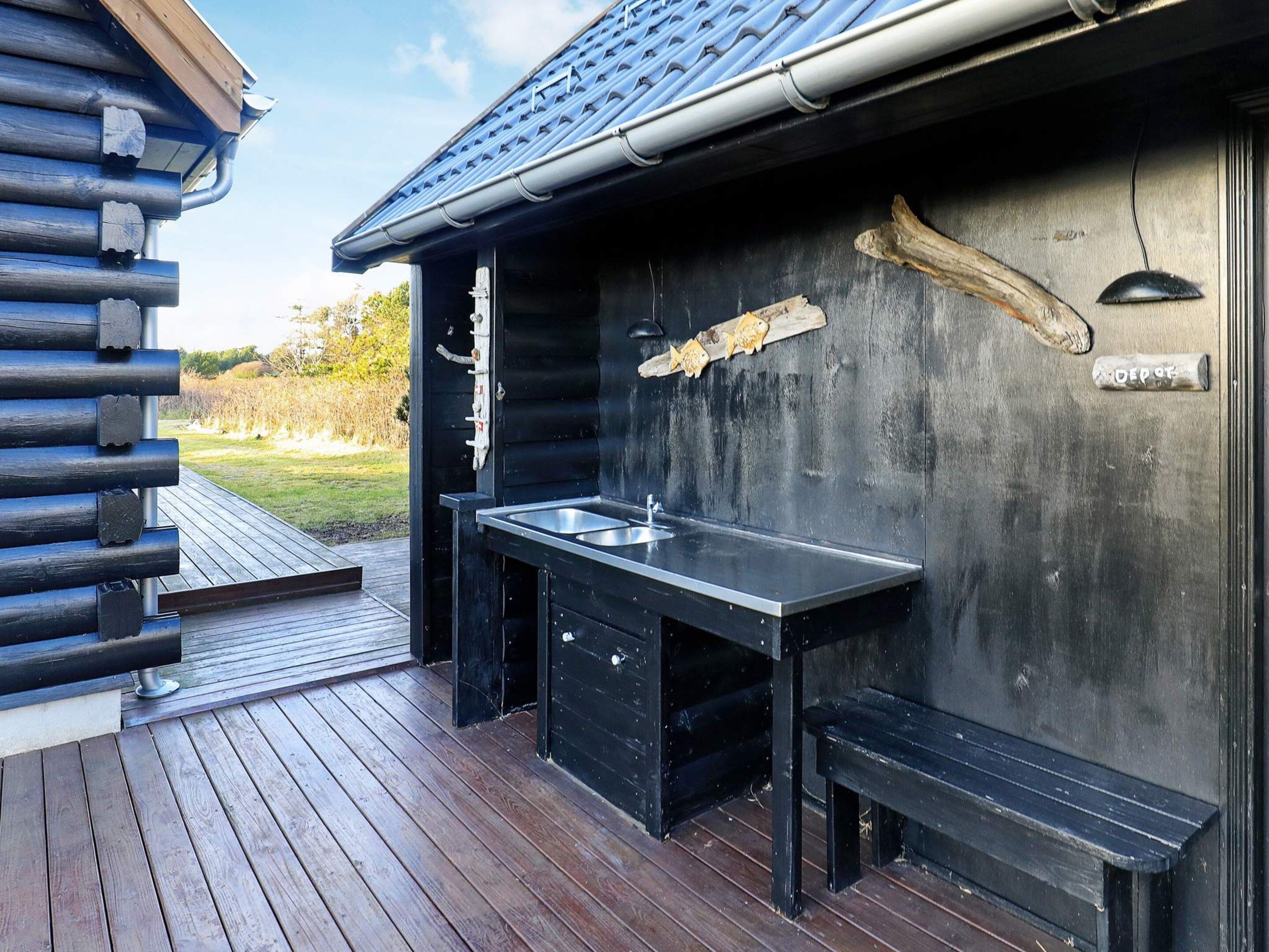 Une terrasse en bois dotée d’une cuisine extérieure noire, comprenant un évier et un banc.