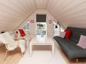 A cozy attic room with a white table, a grey sofa, and a white chair with a red cushion.