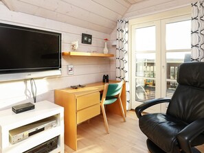 A room with a flat-screen TV, wooden desk, a chair, a black leather chair, and a view through a glass door.