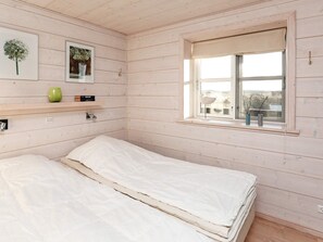 A room with a bed, a window, and a shelf with books and a vase.
