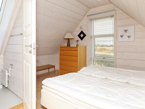 A bedroom with a sloped ceiling, a bed, a dresser, a bench, and a window with blinds.