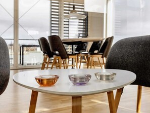 A round table with three glass bowls in different colors, surrounded by chairs and a dining table in the background.