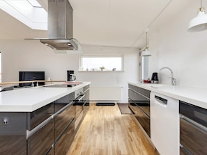 A modern kitchen with a central island, stainless steel appliances, and a window providing natural light. - 5 Person Holiday Home in Stege (Stege)