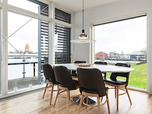 Área de refeições moderna com mesa redonda, cadeiras pretas e vista para um rio e edifícios.