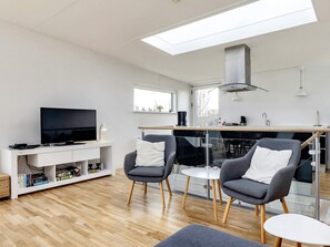 Een moderne woonkamer met een flatscreen televisie, twee grijze fauteuils, een klein witte tafel en een houten vloer.