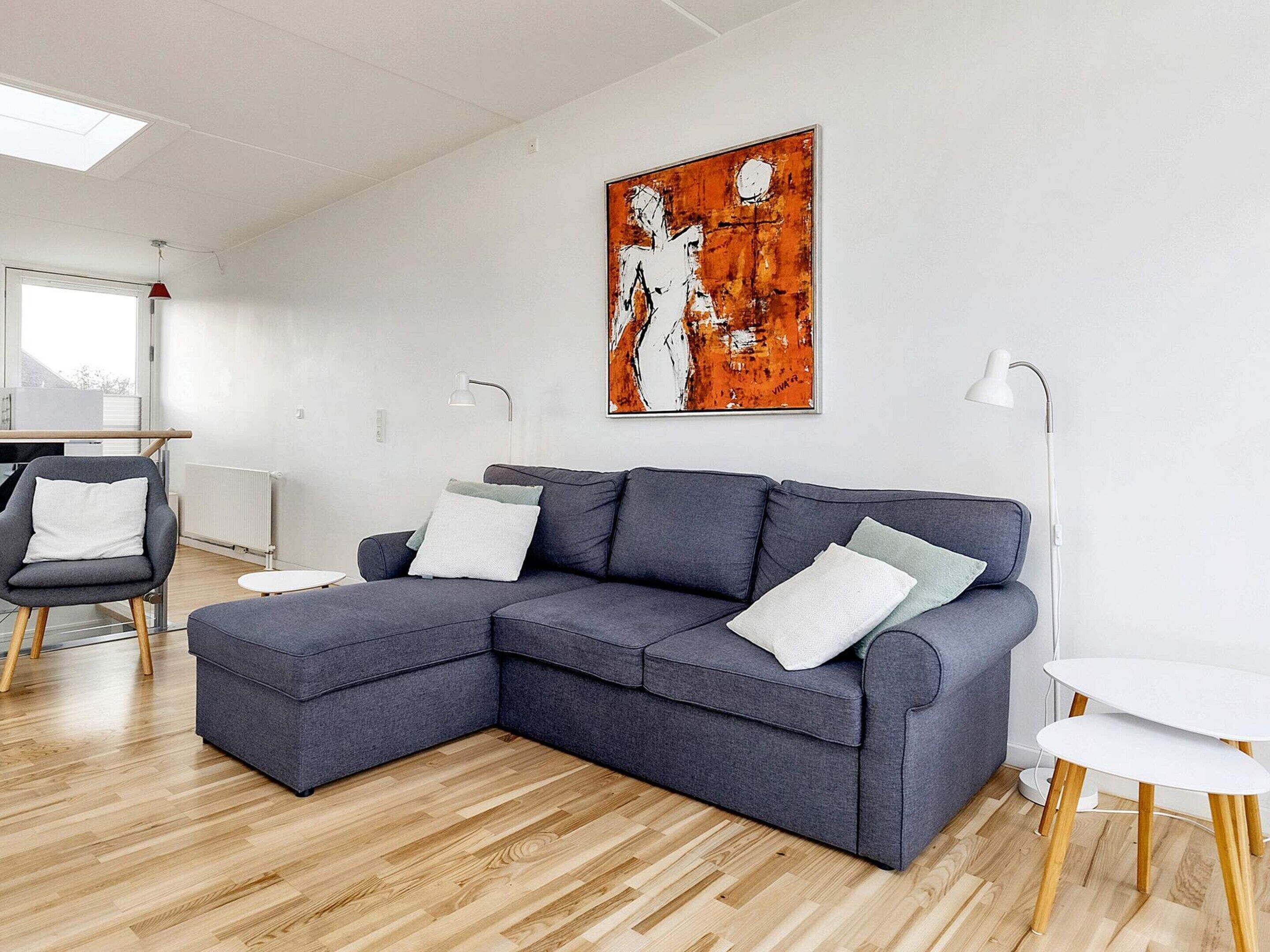 A modern living room with a grey sectional sofa, a small round table, and a painting on the wall.