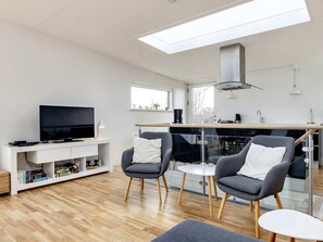 A modern living room with a flat-screen TV, a white entertainment unit, and two grey armchairs with white cushions.