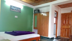 Una habitación con una cama, un armario de madera, un televisor en una estantería y una pared verde.