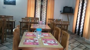 Un comedor con una mesa dispuesta para cuatro personas, rodeada de sillas de madera, un piso de baldosas y un televisor sobre un mueble contra la pared.