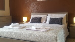 A neatly made bed with white linens and pillows, two bedside lamps, and a wooden nightstand.