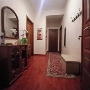 A hallway with a wooden floor, a bench, a mirror, a door, and a wall-mounted coat rack.