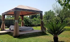 A gazebo with a covered seating area and a small table, surrounded by grass and trees.