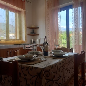 A dining area with a table set for two, a bottle of wine, and a view of the outdoors.