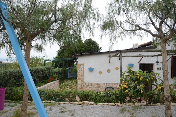 A rustic house with a stone facade, a small garden with a pergola, and a tree with yellow fruits.