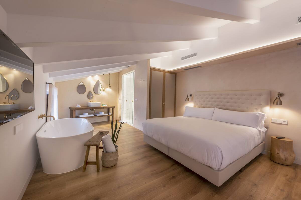 Un dormitorio moderno con una cama grande, una bañera independiente y un tocador con espejo.