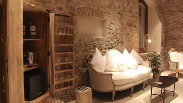 Una sala de estar acogedora con una pared de piedra, un sofá blanco, un aparador de madera con cristalería y una mesita con una planta.
