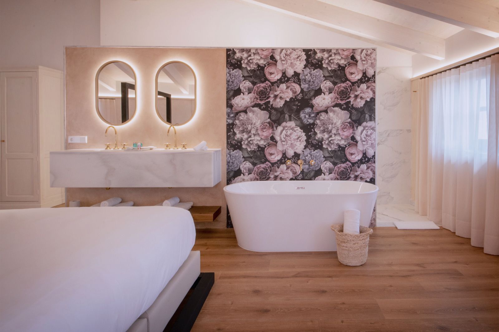 A modern bathroom with a freestanding bathtub, a double vanity with two mirrors, and a floral wallpaper backdrop.