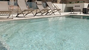 A clear pool with lounge chairs, a stone building with a tower, and a cross on top. - Palau Macelli (Castello d'Empuries)