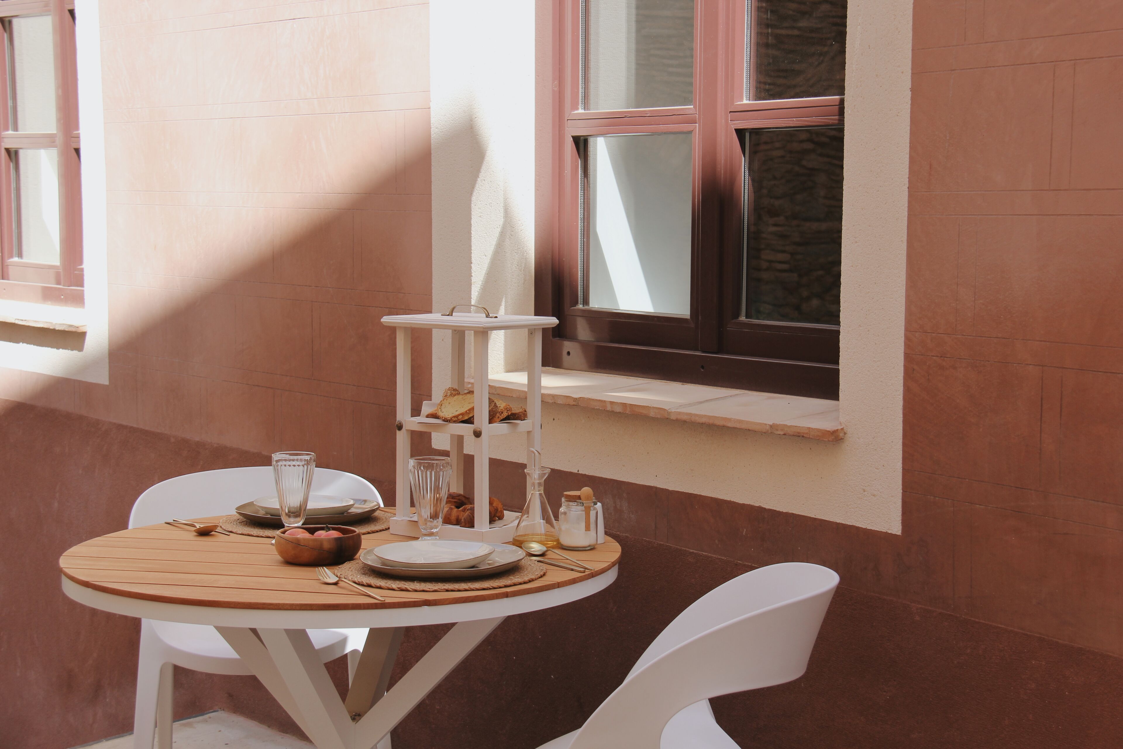 Une table ronde avec une chaise blanche, une petite étagère blanche sur laquelle se trouve du pain, ainsi que divers aliments pour le petit-déjeuner.