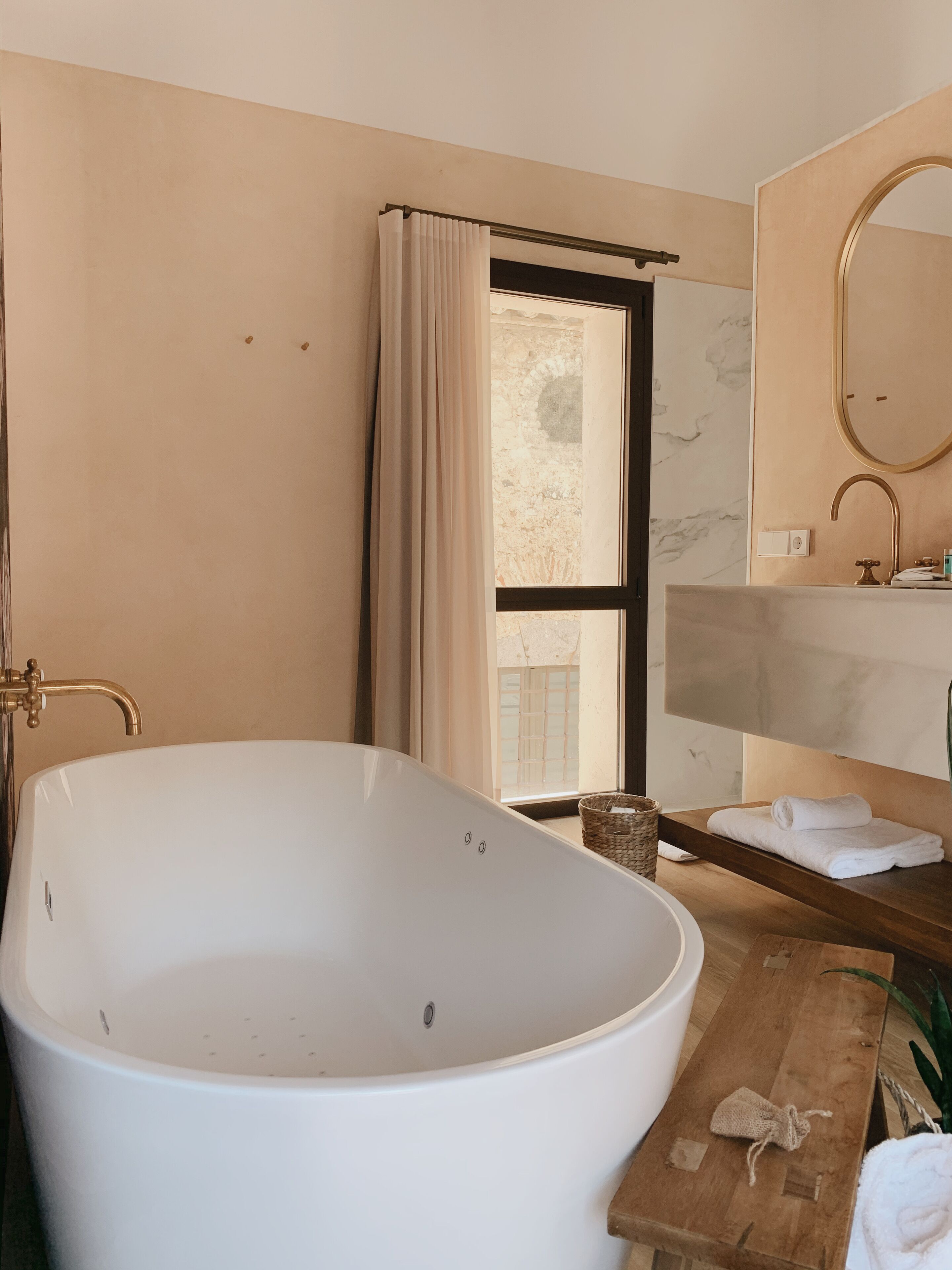Un baño con una bañera independiente, un tocador de madera con espejo y una ventana con cortinas.