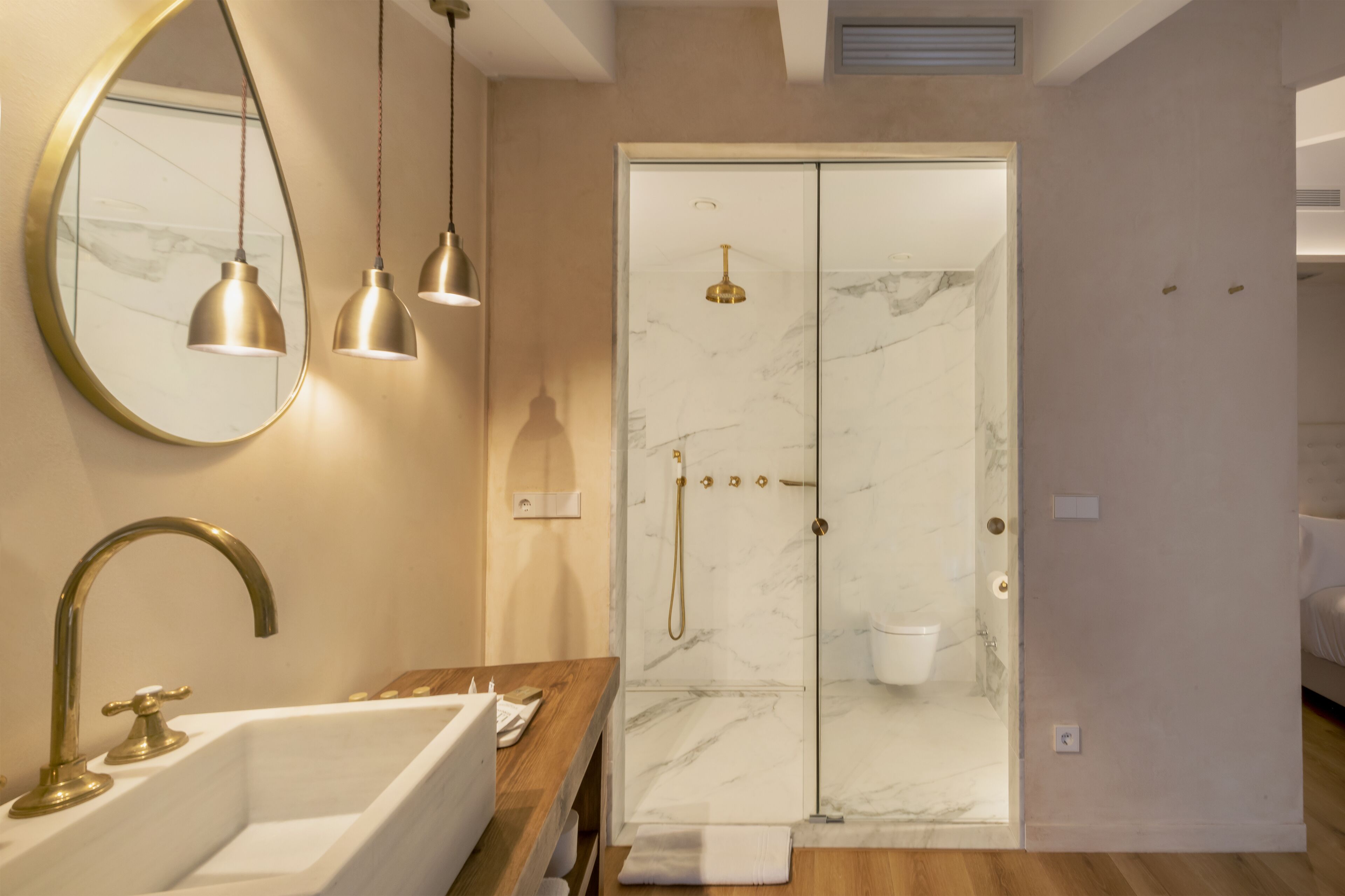 A modern bathroom with a marble shower, a sink with a gold faucet, and pendant lights.