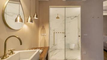 A modern bathroom with a marble shower, a sink with a gold faucet, and pendant lights.