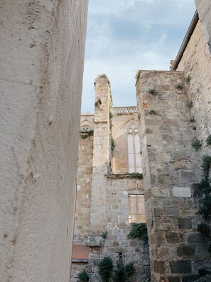 Una calle estrecha con edificios de piedra, uno con un arco visible y otro con un muro de piedra.