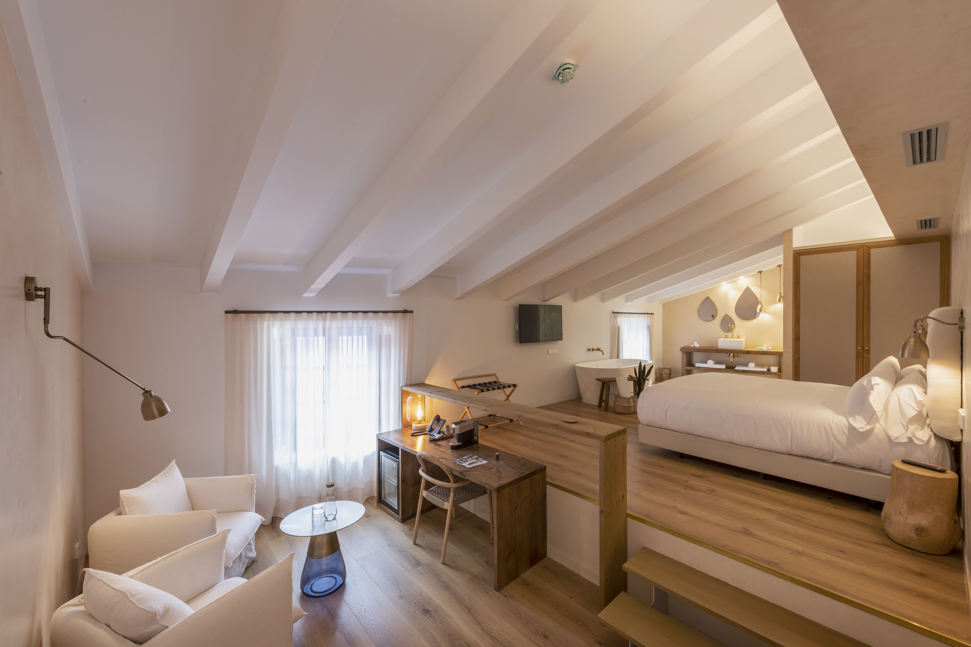 A modern hotel room with a wooden desk, a sofa, a bed, and a TV.