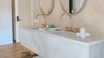 Un baño moderno con un tocador amplio, dos espejos con marcos dorados, un lavamanos blanco y un estante de madera con toallas.