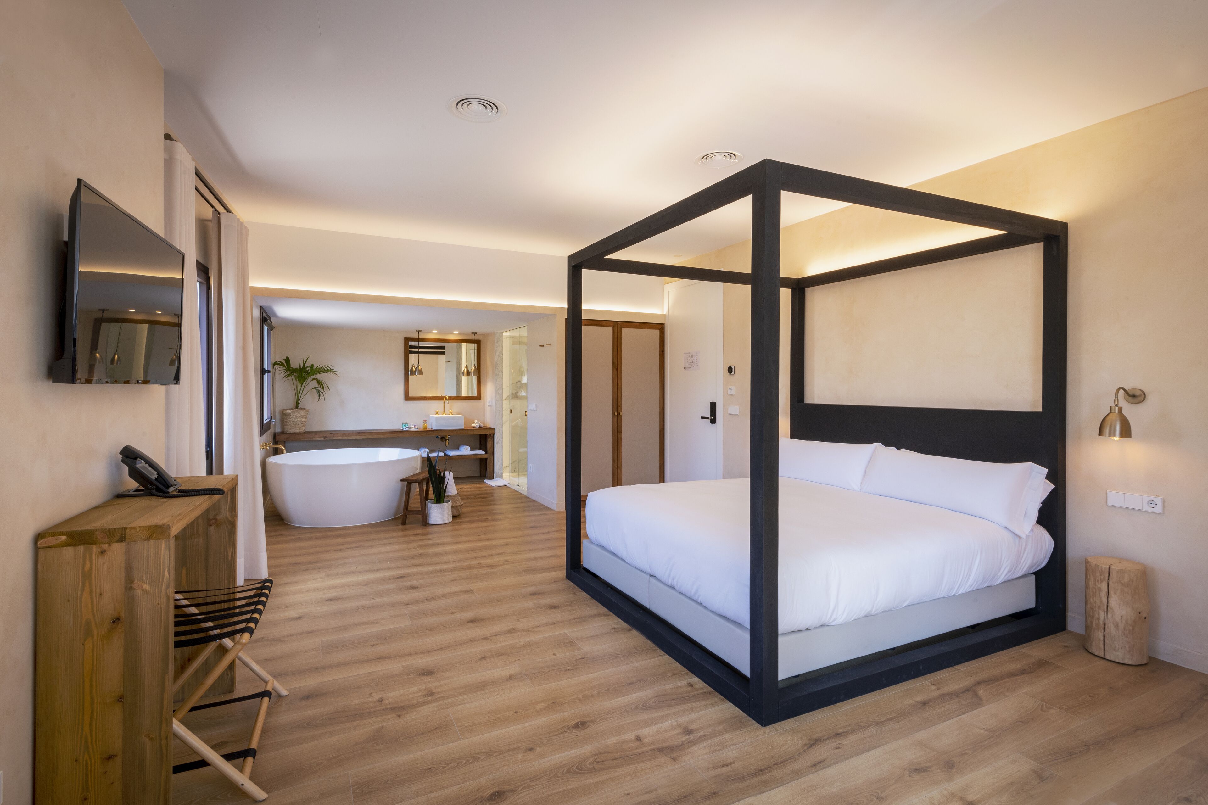 Ein modernes Schlafzimmer mit einem Himmelbett, einem Holztisch, einer großen Badewanne und einem Spiegel.