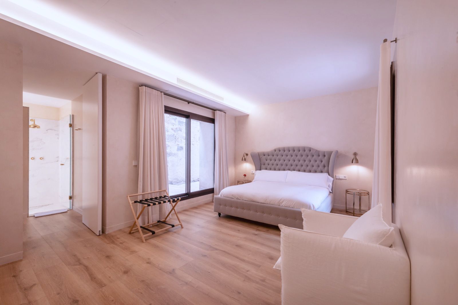 Un dormitorio con una cama grande, una mesita de noche, un perchero y una ventana con cortinas.