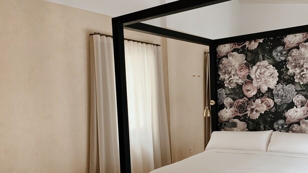 A bedroom with a large bed, a bedside table, and a headboard with floral wallpaper. - Palau Macelli (Castello d'Empuries)