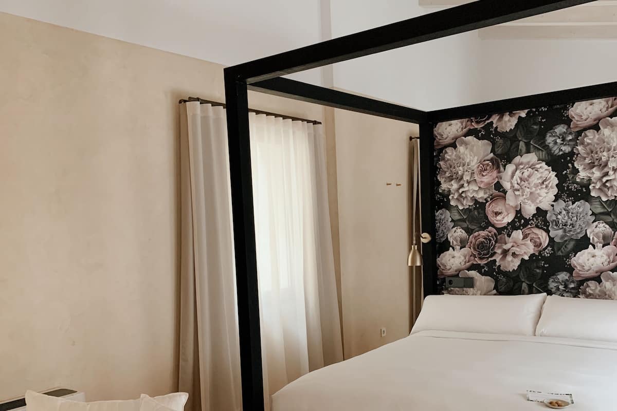 Un dormitorio con una cama grande, una mesita de noche y un cabecero con papel tapiz floral.