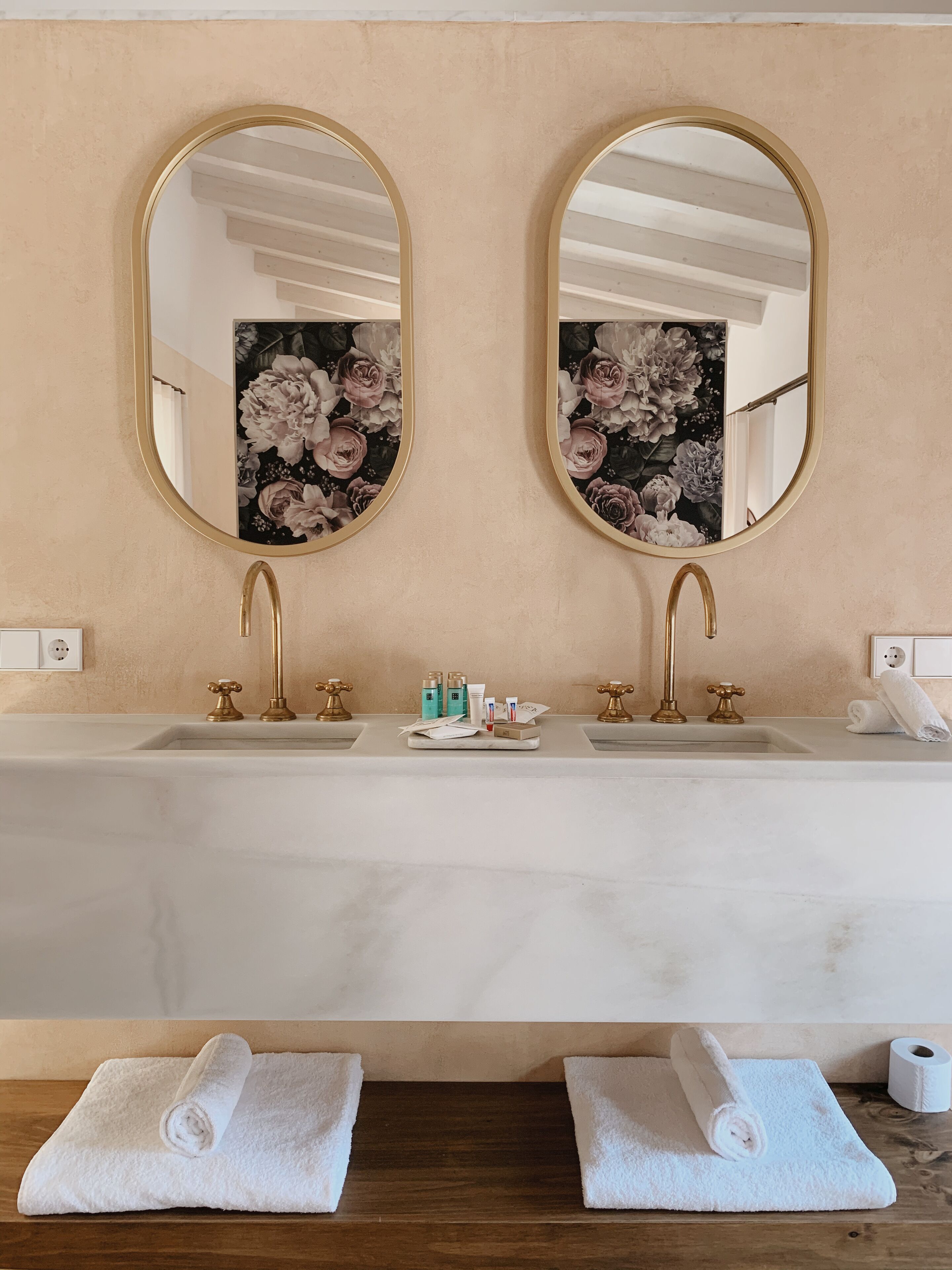 Un baño con dos lavamanos, grifos dorados y un espejo con diseño floral.