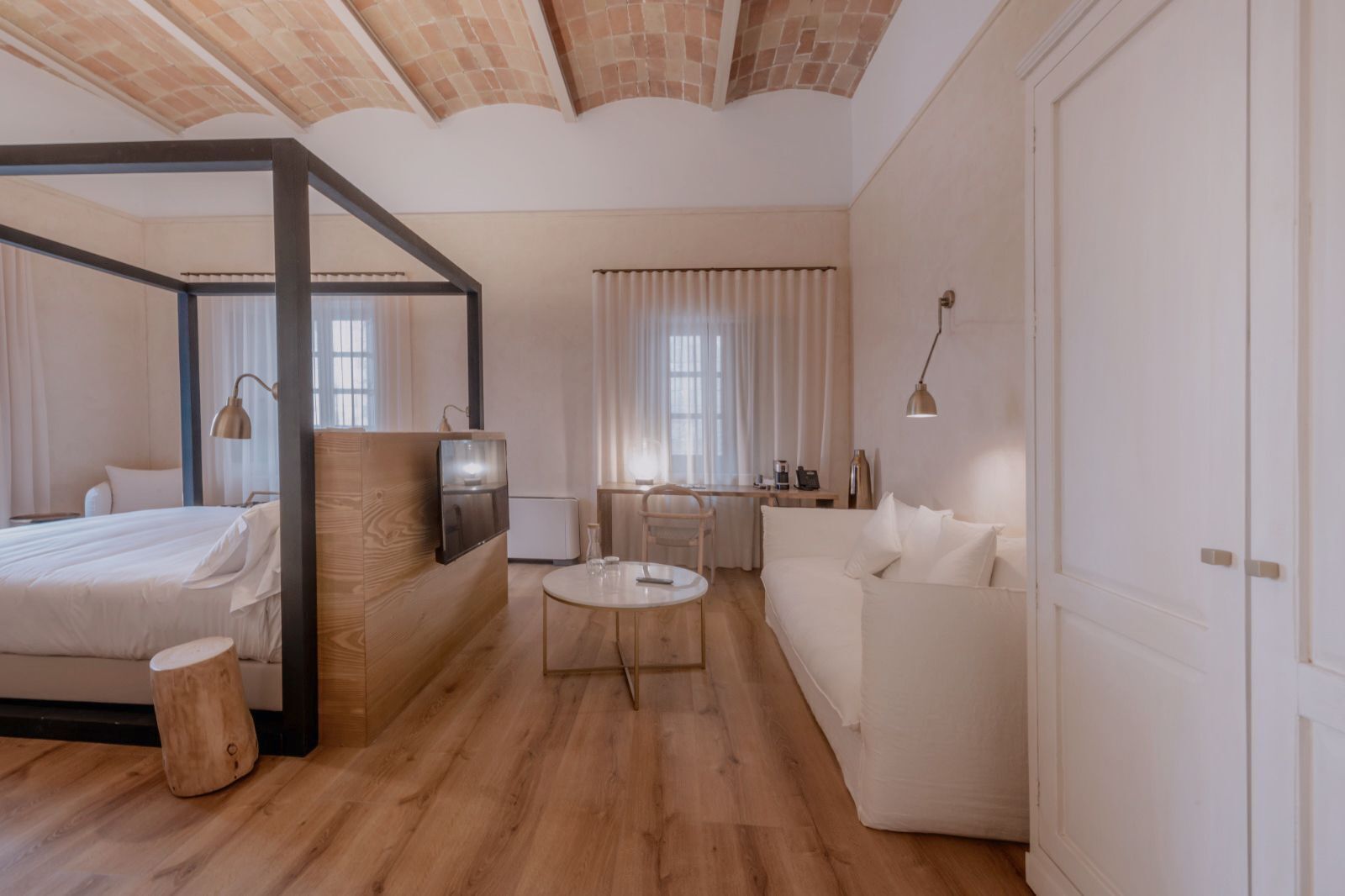 Un dormitorio moderno con una cama con dosel, una mesita redonda y un sofá.