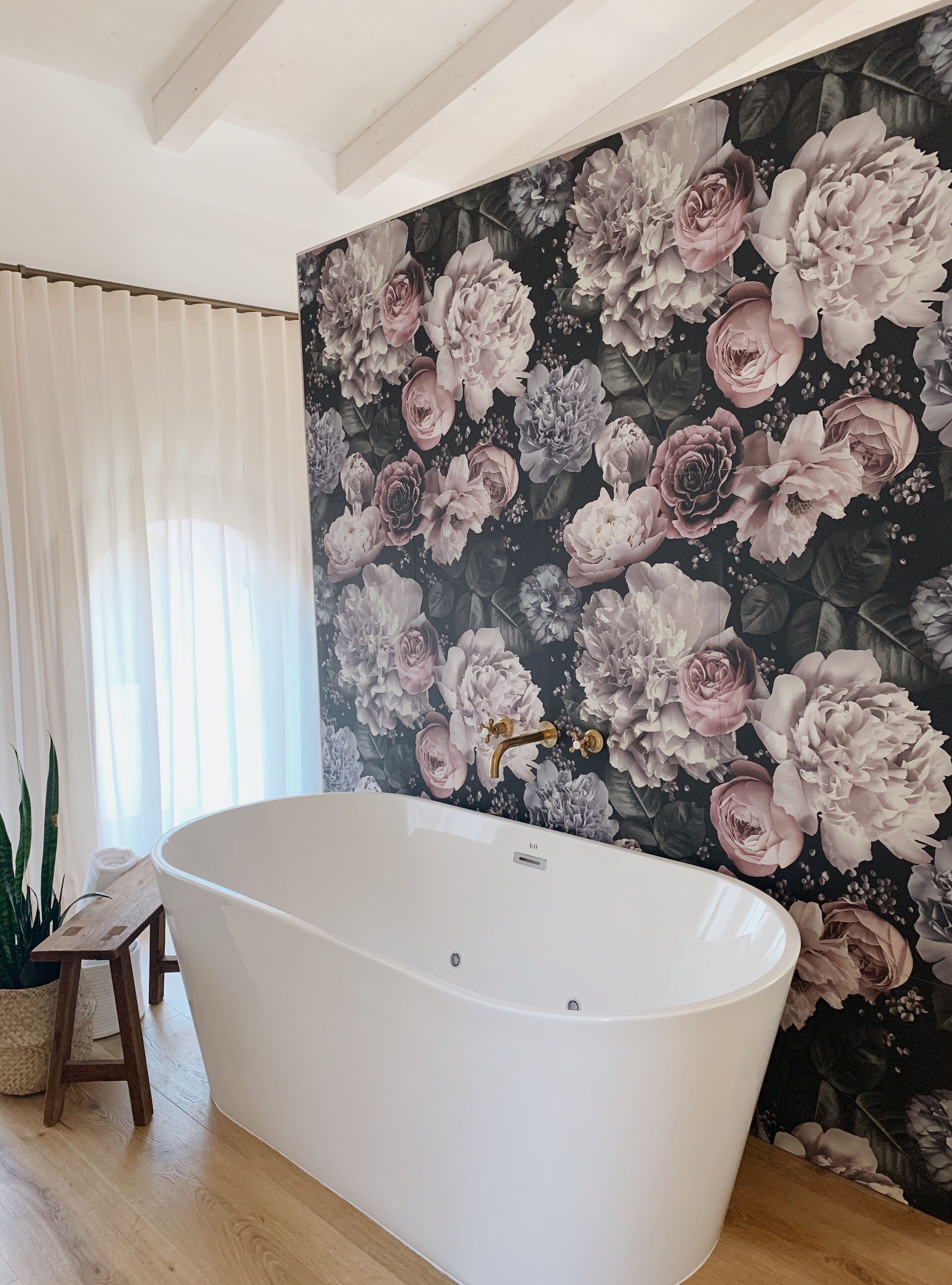 Un baño con una bañera independiente, un papel tapiz floral y suelo de madera.