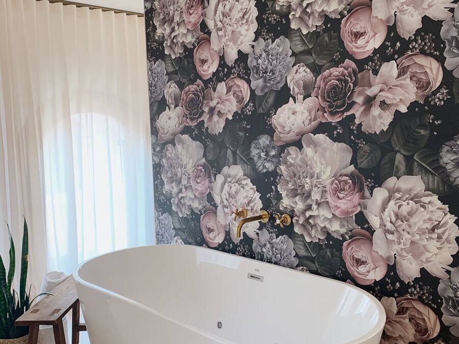 Un baño con una bañera independiente, un papel tapiz floral y suelo de madera.