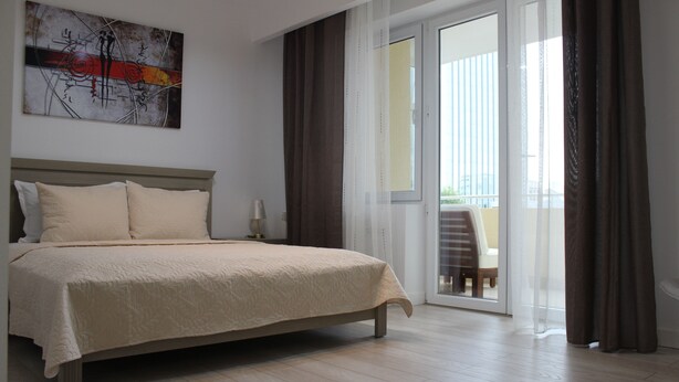 Ein Schlafzimmer mit einem Bett, einem Bild an der Wand und Blick ins Freie durch eine Schiebetür.