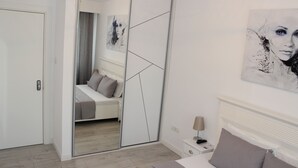 Ein modernes Schlafzimmer mit einem großen Spiegel, einem Bett mit grauer Bettwäsche, einem Nachttisch mit einer Lampe und Bildern an den Wänden.
