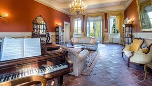 A grand piano, a sofa, and a chandelier in a spacious room with large windows.