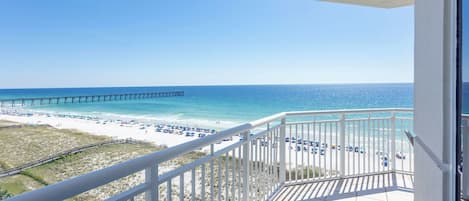 Ein Balkon mit Blick auf einen Strand, einen Steg und einen klaren Himmel.