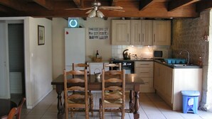 Una cocina con armarios de madera, una mesa de comedor con sillas, un ventilador de techo y un refrigerador.