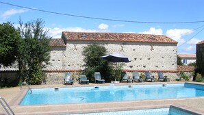 Una piscina con sillas de descanso y sombrillas, rodeada de edificios de piedra con techos de tejas.