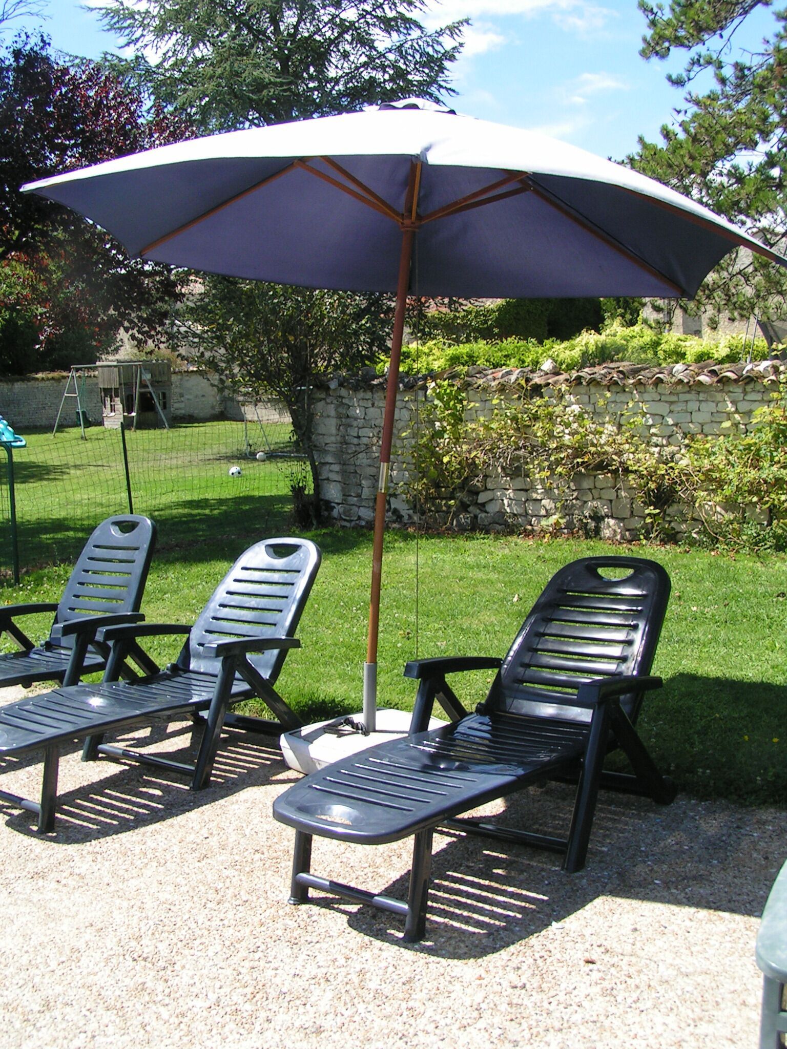 Un espace patio aménagé avec trois chaises longues et un grand parasol.