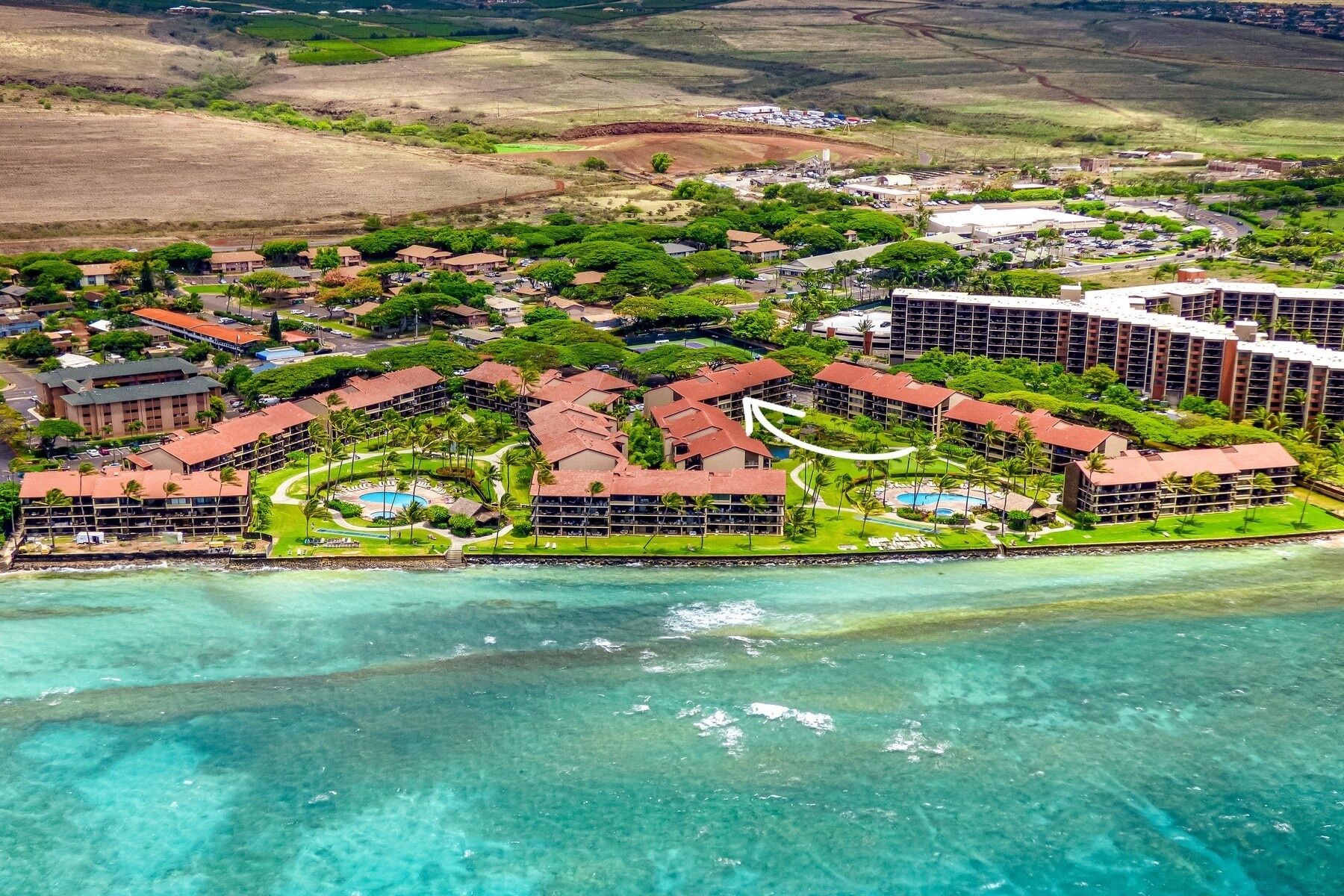 Vista aérea de un resort con varias construcciones, un área de piscina y acceso a la playa.